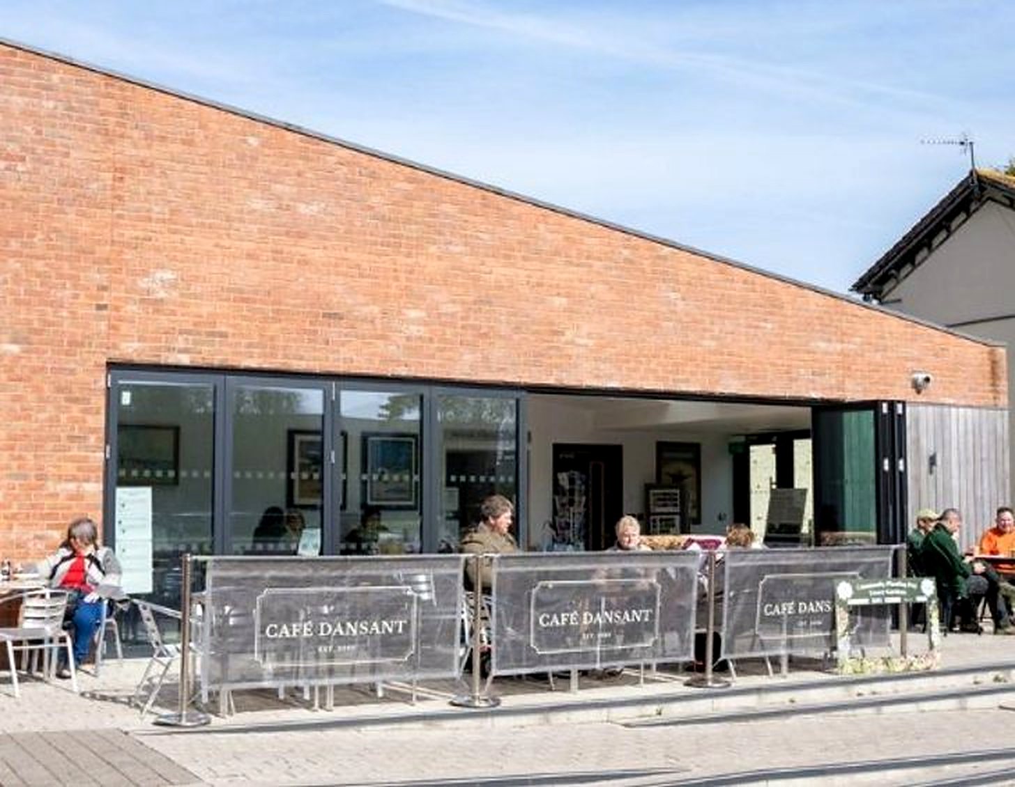 The brick Tower Gardens Pavilion with its glass doors open and people sitting at tables outside